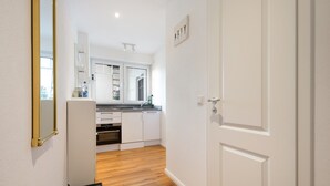 A narrow hallway leading to a kitchen with white cabinets, a countertop, and a window.
