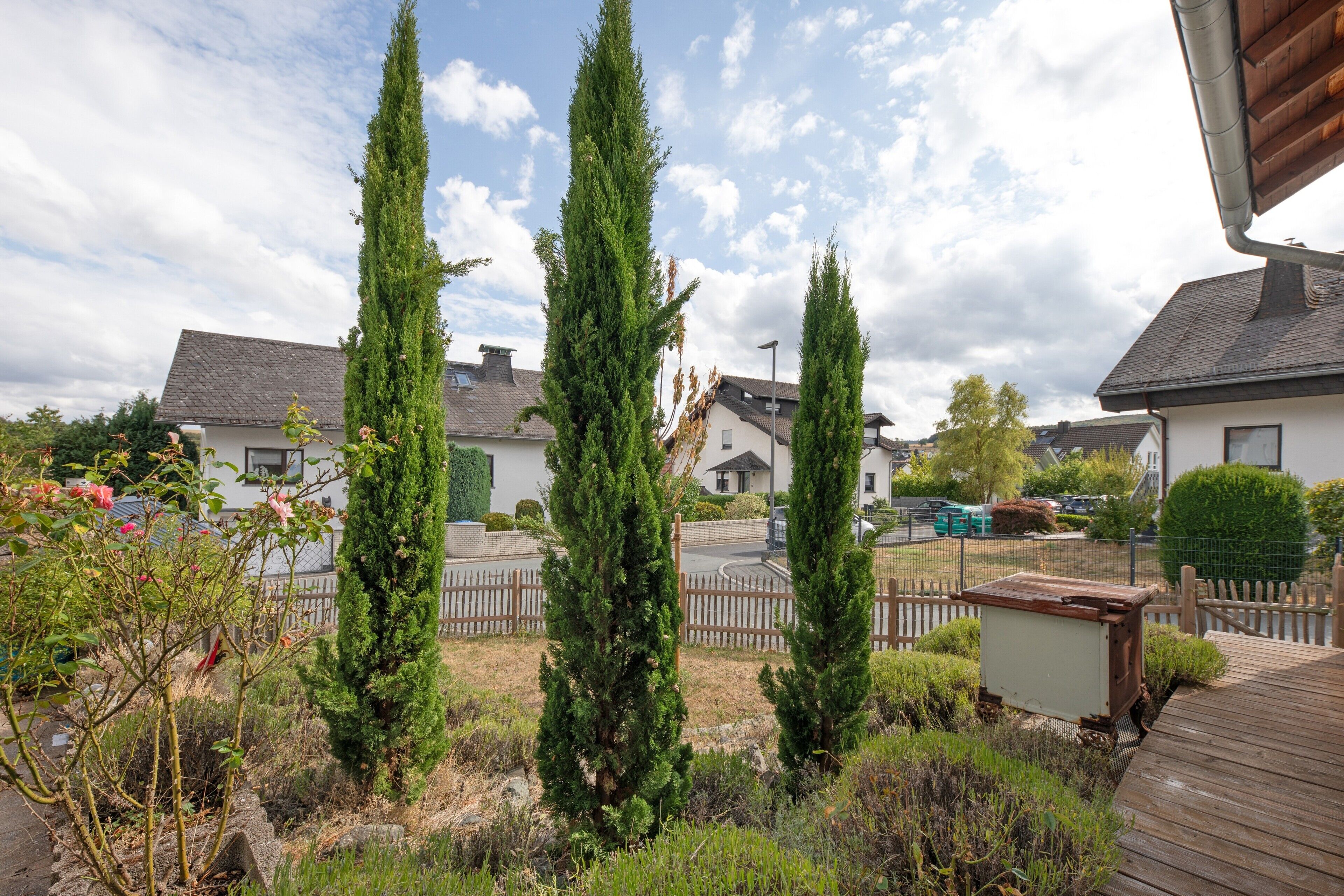 A residential area with multiple houses, a wooden fence, and a variety of trees.