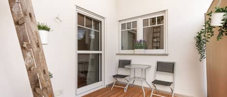 A wooden deck with a white wall, two windows, and a small table with two chairs.