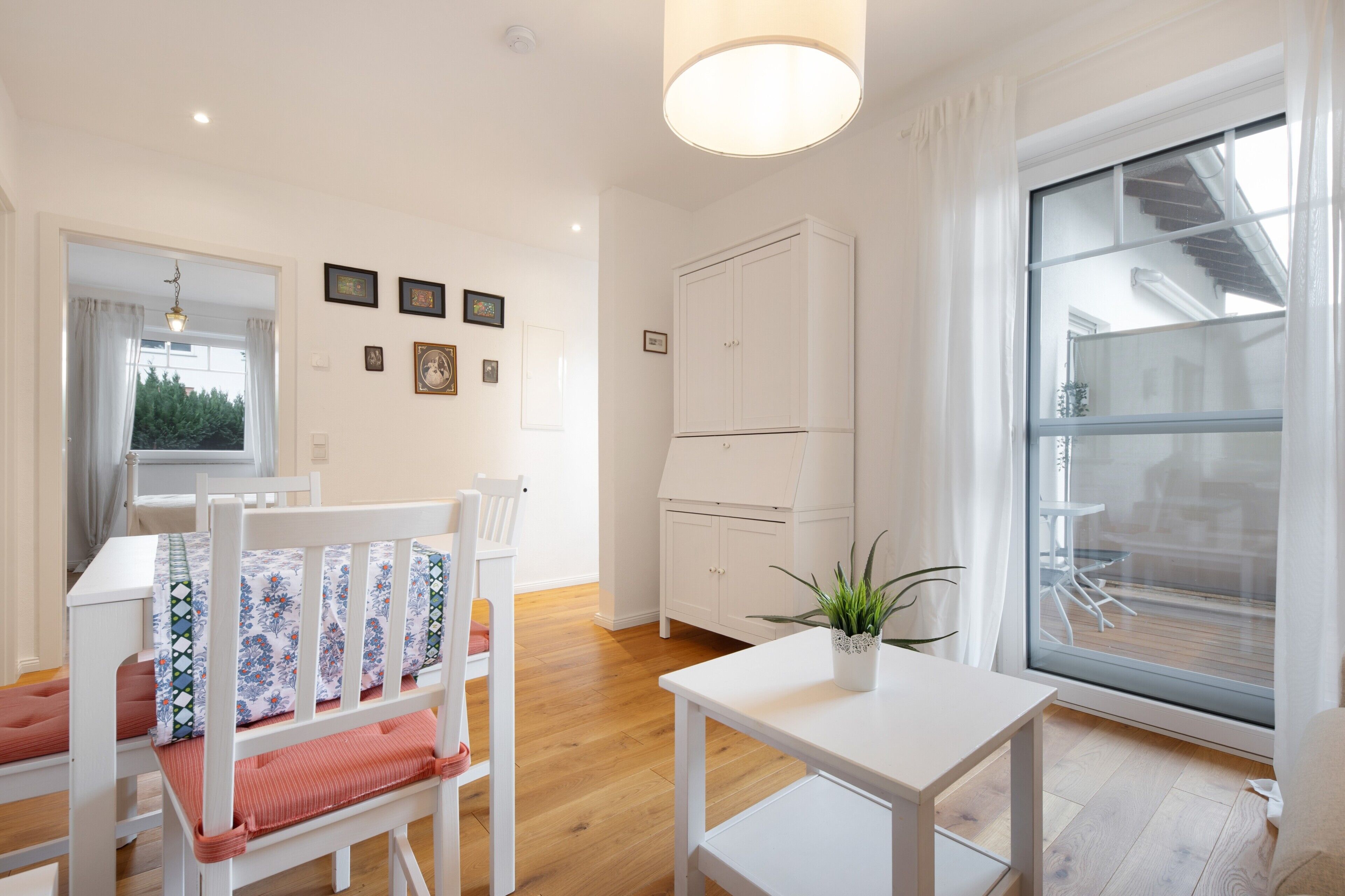 A bright room with a dining table, chairs, a white cabinet, and a large window with a view.