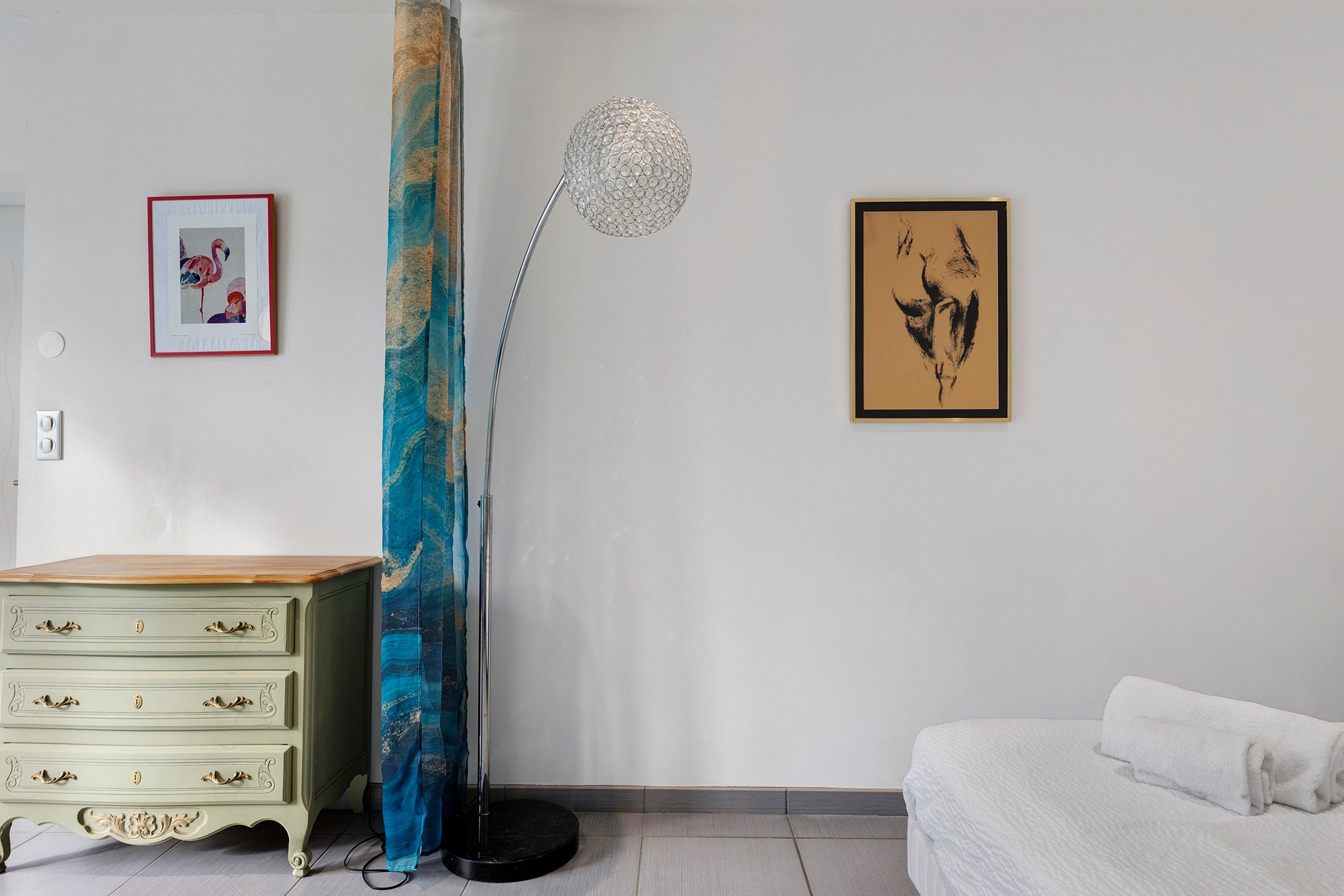 Una habitación con un aparador de madera, una lámpara de pie alta y dos cuadros en la pared.