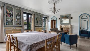 A spacious room with a large dining table, bookshelves, a sofa, and a fireplace.