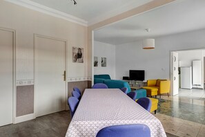 A modern living room with a sofa set, a television, and a dining area with a patterned tablecloth. - Domaine de Trevety: Private Garden, Balcony & Wi-Fi, Ideal for Families & Groups (Châtillon-sur-Cher)