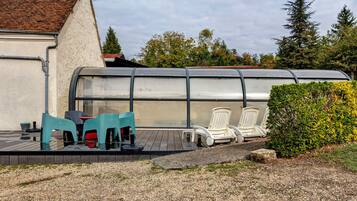 A covered outdoor seating area with chairs and tables, a gravel path, and a building with a tiled roof.