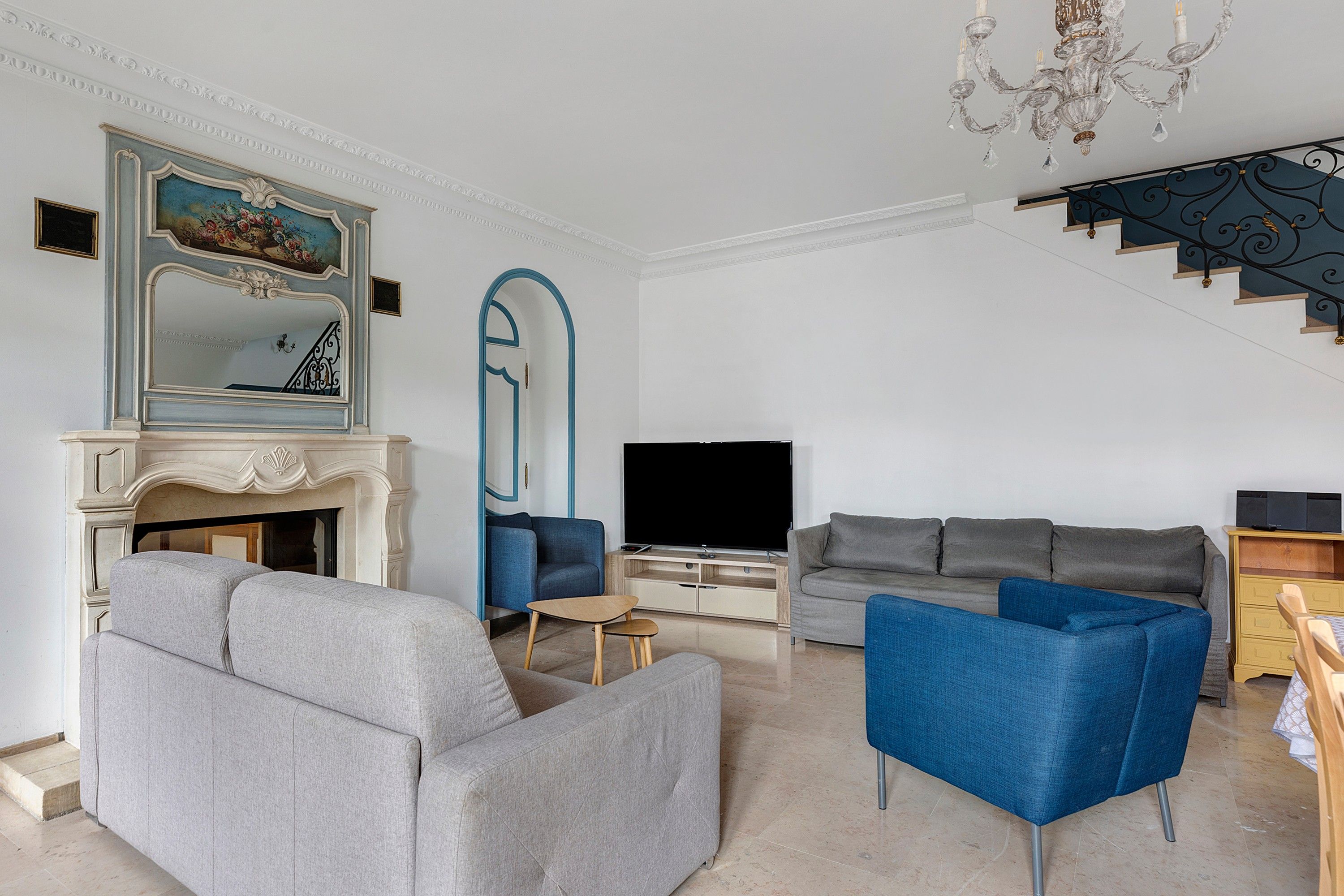 Ein Wohnzimmer mit Kamin, Fernseher, Treppe und einem blauen Sessel.