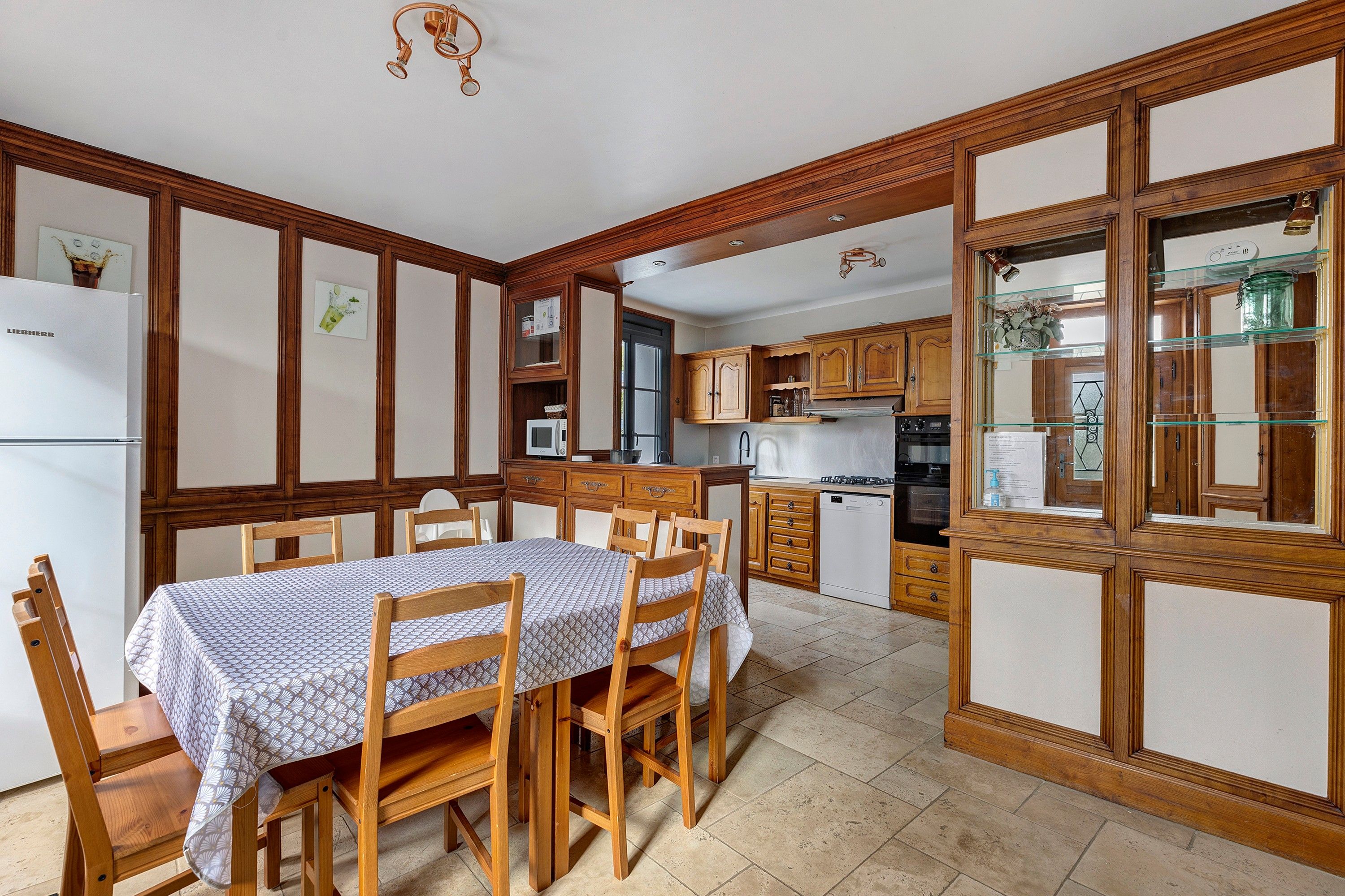 A kitchen with wooden cabinets, a dining table with chairs, and a refrigerator.