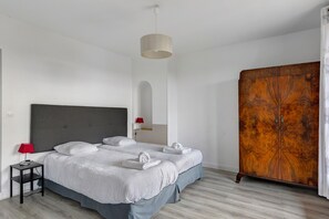 A hotel room with a bed, a small table, a red lamp, a wardrobe, and a hanging light fixture. - Domaine de Trevety: Private Garden, Balcony & Wi-Fi, Ideal for Families & Groups (Châtillon-sur-Cher)