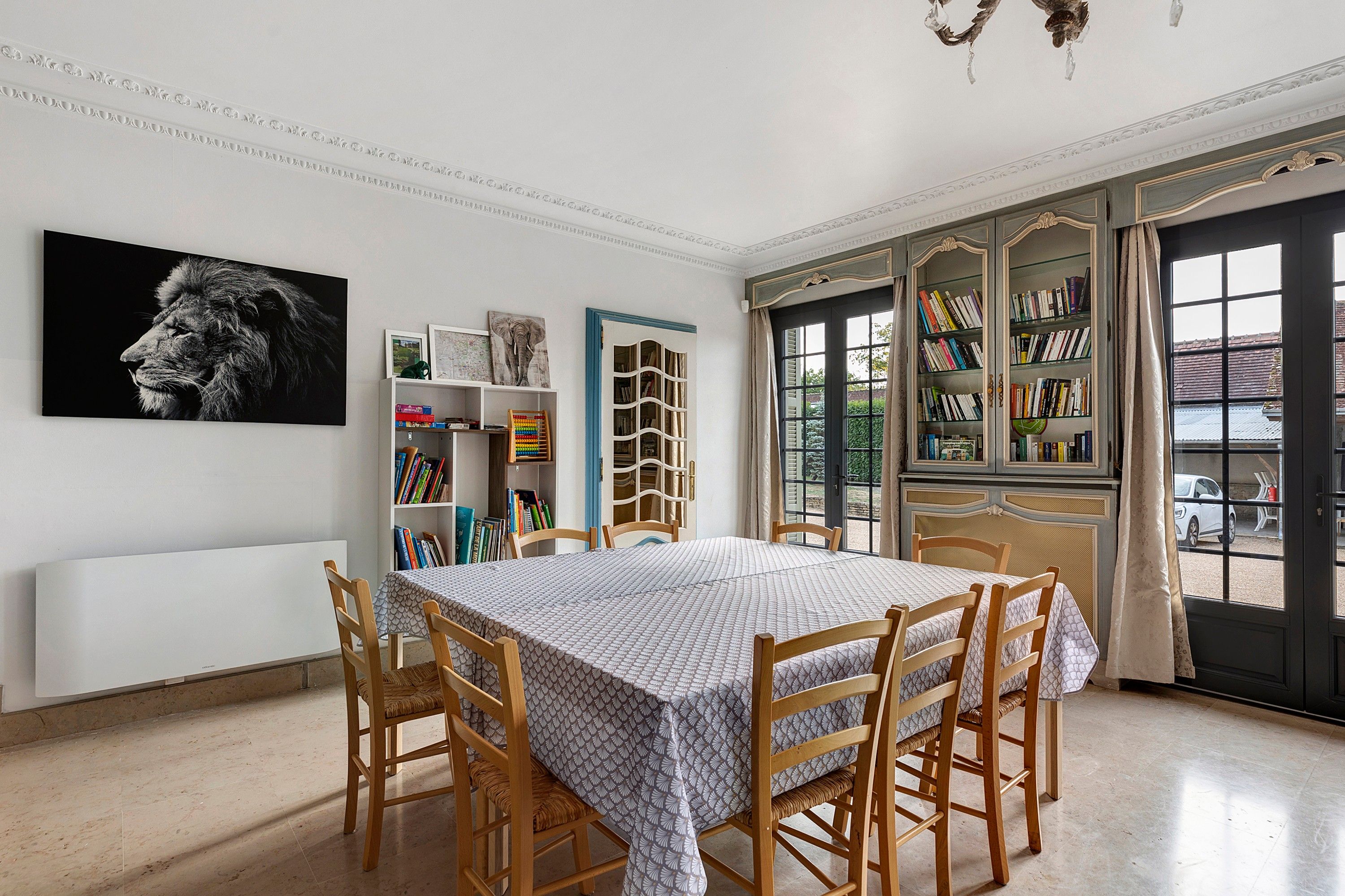 A dining room with a table and chairs, a bookshelf, and a large window with bookshelves.