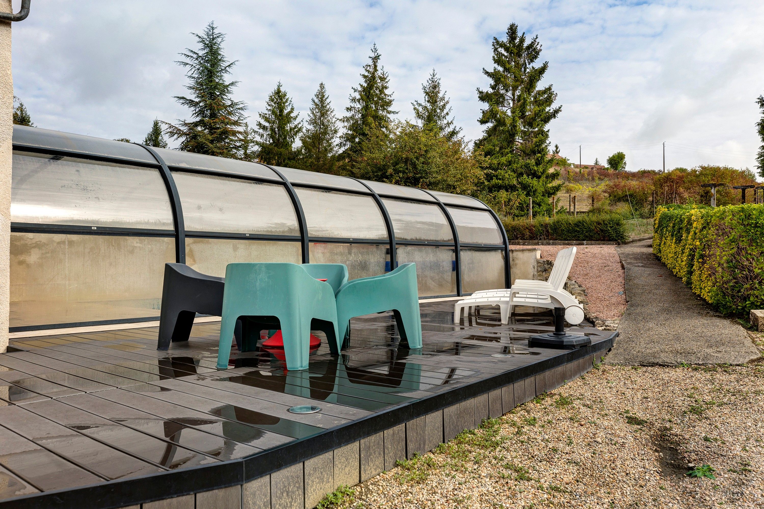 A covered outdoor area with a pool, seating, and a view of trees.