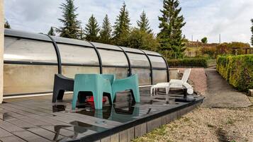 A covered outdoor area with a pool, seating, and a view of trees.