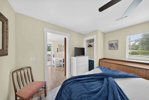 A bedroom with a bed, a TV, a chair, and a window with blinds.