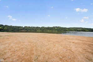 A sandy beach with a calm lake and a forested hill in the background.