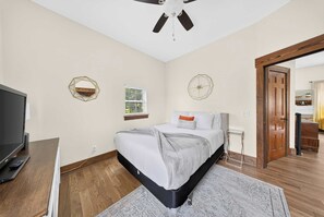 Een slaapkamer met een bed, een televisie, een plafondventilator en een houten vloer.