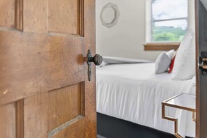 A wooden door with a round handle and a keyhole, leading to a bedroom with a bed, pillows, and a window with a view. - Monte Ne Lakehouse - Lake View (Rogers)