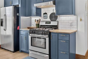 Een moderne keuken met een roestvrijstalen koelkast, een gasfornuis en blauwe kastjes.