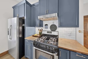 A kitchen with blue cabinets, a stainless steel refrigerator, a gas stove, and a built-in oven. - Monte Ne Lakehouse - Lake View (Rogers)