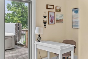 A room with a white table, a chair, and a lamp. There are four framed artworks on the wall.