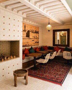 A cozy interior with a brick fireplace, a large mural, and a seating area with tables and chairs. - Elegant 4-Room Riad with Pool – Just Steps from the Royal Palace (Marrakech)