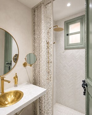 A bathroom with a gold sink, a large mirror, a shower with a window, and a decorative white wall panel. - Elegant 4-Room Riad with Pool – Just Steps from the Royal Palace (Marrakech)