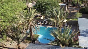 Zona de piscina con sillones de descanso, palmeras y vistas a un área residencial.