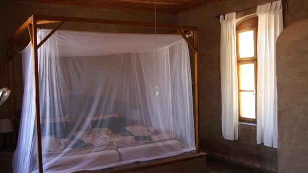 Una habitación con una cama con dosel, una ventana con cortinas y suelo de piedra.