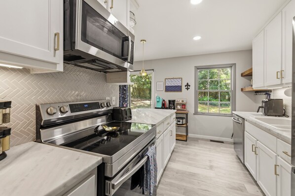 A modern kitchen with stainless steel appliances, a herringbone tile backsplash, and a view of the outdoors.