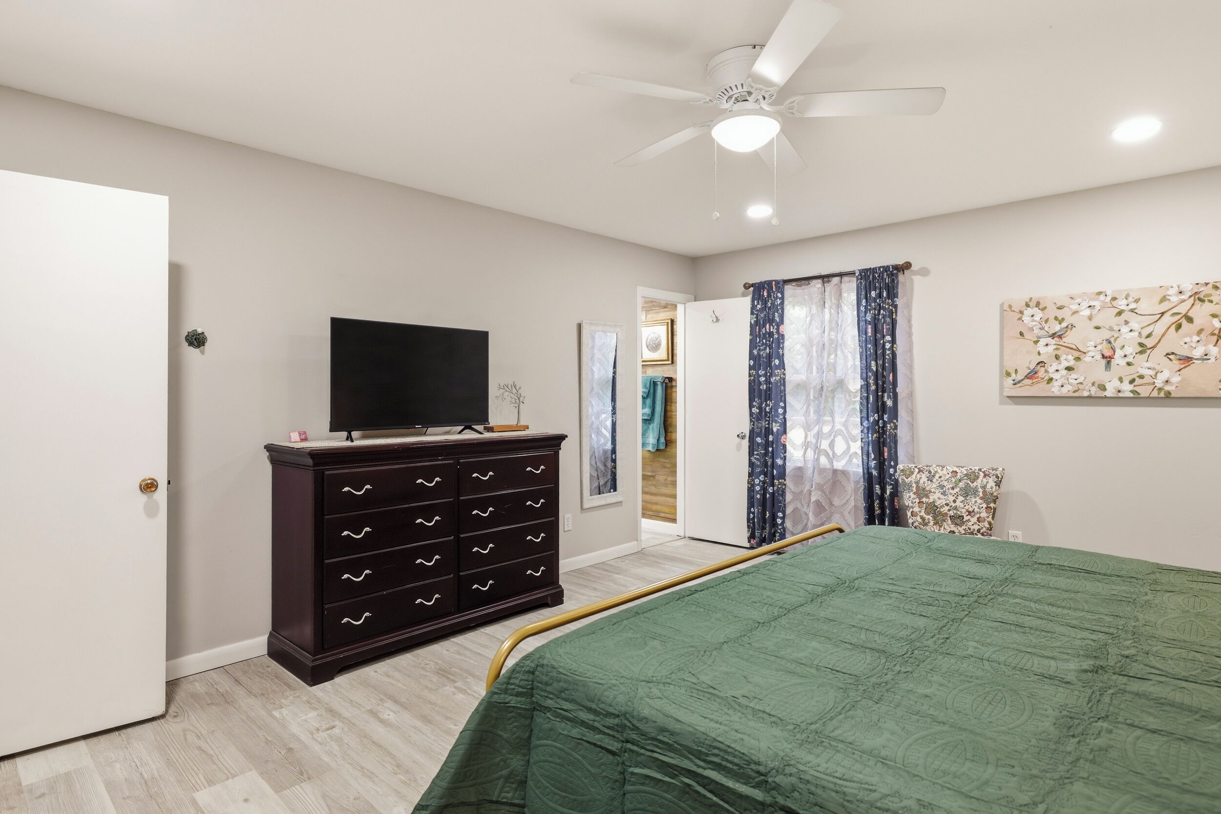 A bedroom with a bed, a dresser, a ceiling fan, and a television.