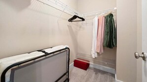 Pieni, käytännöllinen huone, jossa on metallinen sängynrunko, metallinen hylly ja punainen säilytyslaatikko.