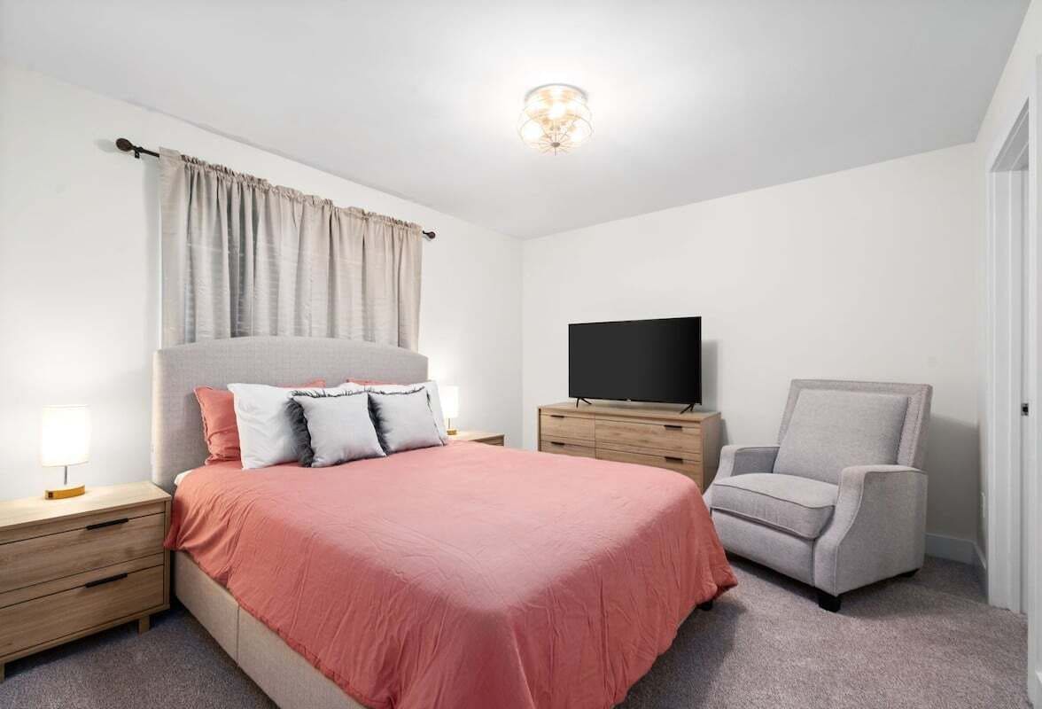 A bedroom with a bed, a TV, a chair, and a nightstand.