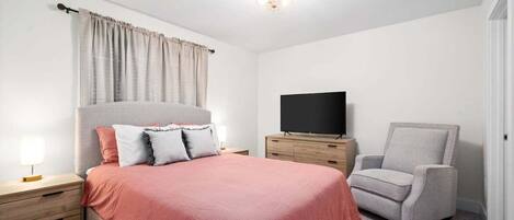 A bedroom with a bed, a TV, a chair, and a nightstand.