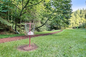A disc golf course with a metal basket on a red pole, surrounded by a grassy area and trees.