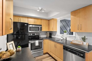 A modern kitchen with stainless steel appliances, wooden cabinets, and a black countertop. - The Lofts of Downtown (540 N 2nd St, #202) | Charming 2-Bedroom in the Heart of Clarksville, TN (Clarksville)