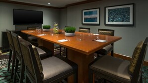 A conference room with a long wooden table, six chairs, a flat-screen TV, and framed artwork on the walls.