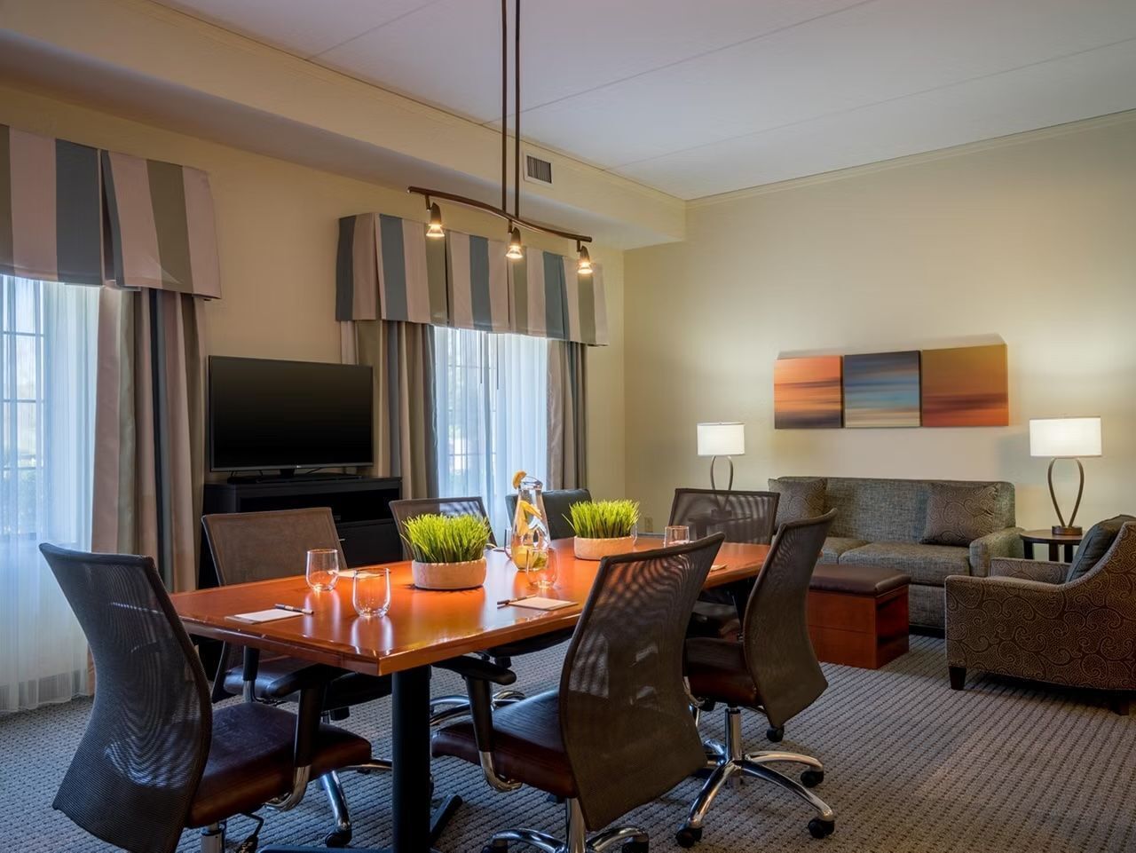 Une chambre d’hôtel équipée d’une table à manger, de chaises, d’un canapé, d’une télévision et d’un tableau au mur.