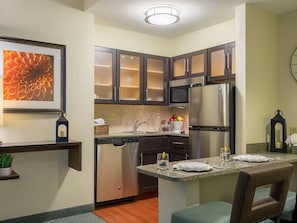 A compact kitchen with dark cabinets, a stainless steel refrigerator, and a dining area with a table and chairs.
