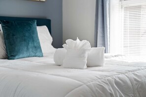 Un lit bien fait, avec du linge de lit blanc et un coussin de couleur turquoise.