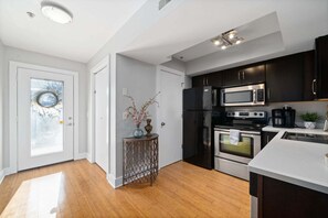 Une cuisine moderne avec des meubles de couleur sombre, des appareils en acier inoxydable et un plan de travail blanc.