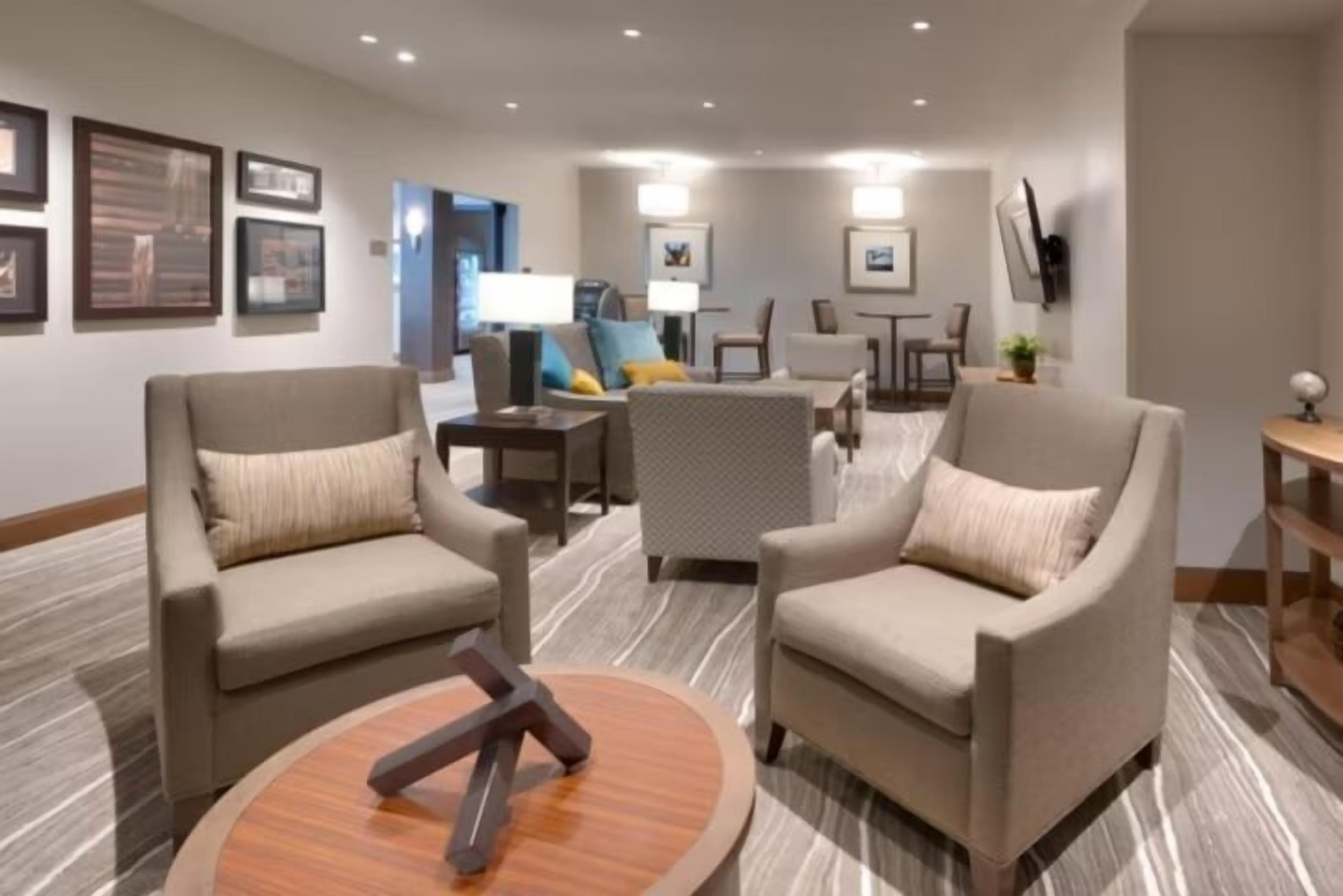 Un hall d’hôtel avec deux fauteuils, une table basse ronde et un téléviseur fixé au mur.