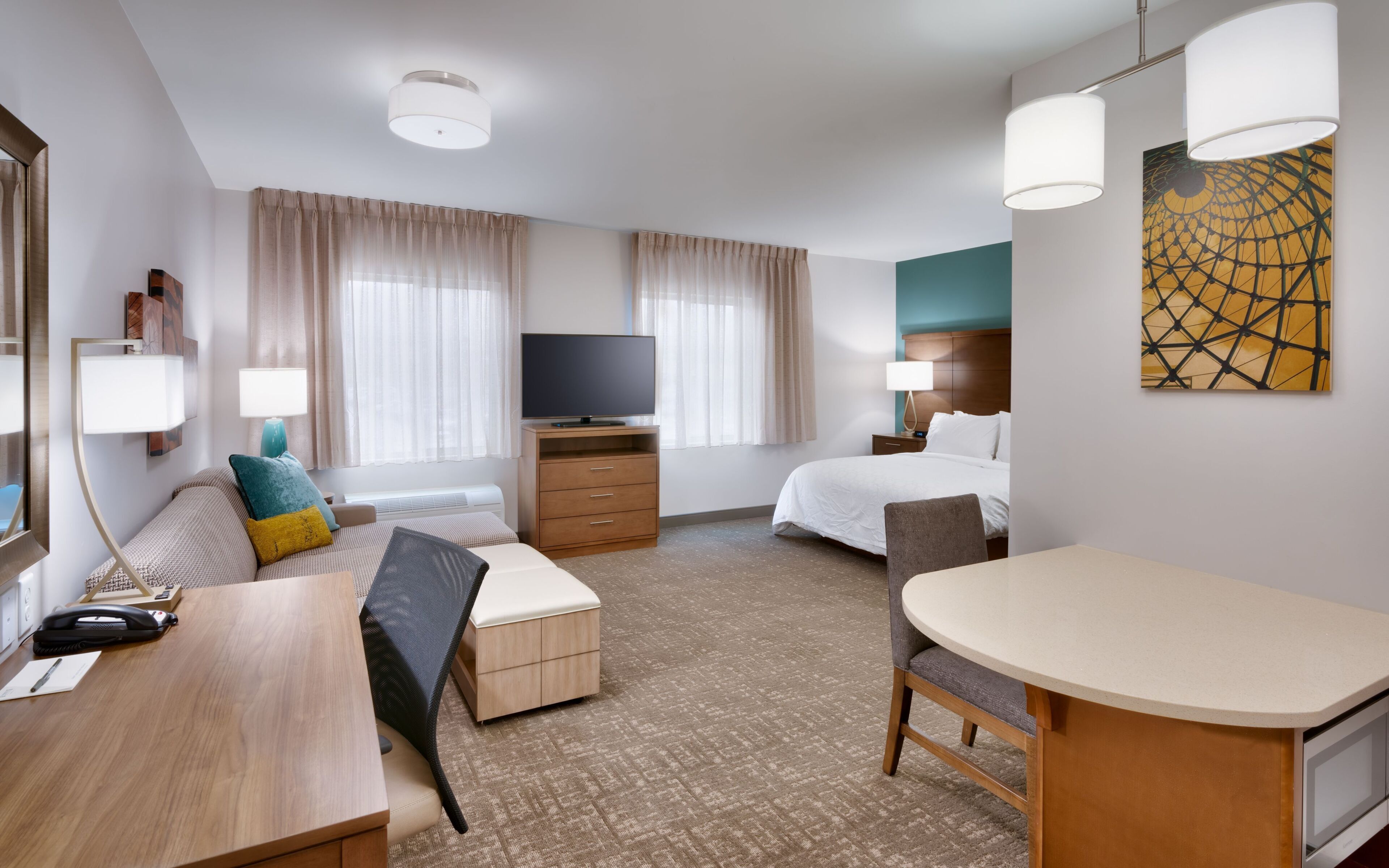 A hotel room with a bed, a desk, a chair, a television, and a painting on the wall.