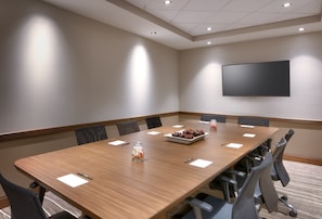Una sala de conferències amb una taula llarga, cadires, un televisió de pantalla plana i un petit objecte decoratiu sobre la taula.