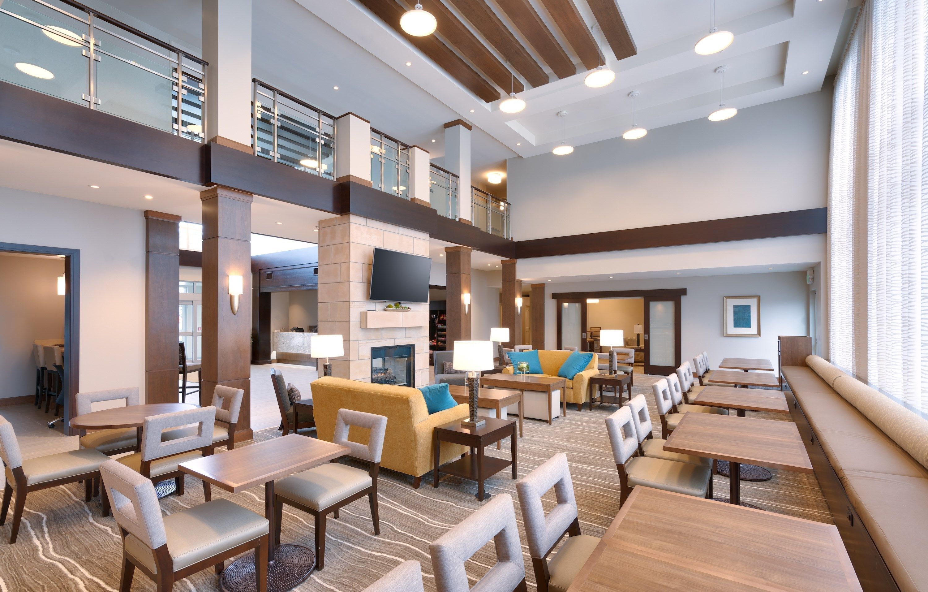 Un hall d’hôtel spacieux doté de plusieurs espaces de détente, notamment des canapés et des tables, et d’un plafond haut avec des poutres apparentes.
