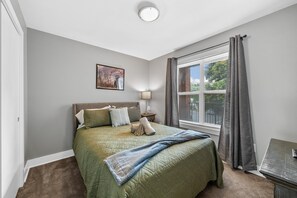 A bedroom with a bed, a nightstand, a lamp, a window with curtains, and a painting on the wall. - The Lofts of Downtown (540 N 2nd St, #201) | Charming 2-Bedroom in the Heart of Clarksville, TN (Clarksville)