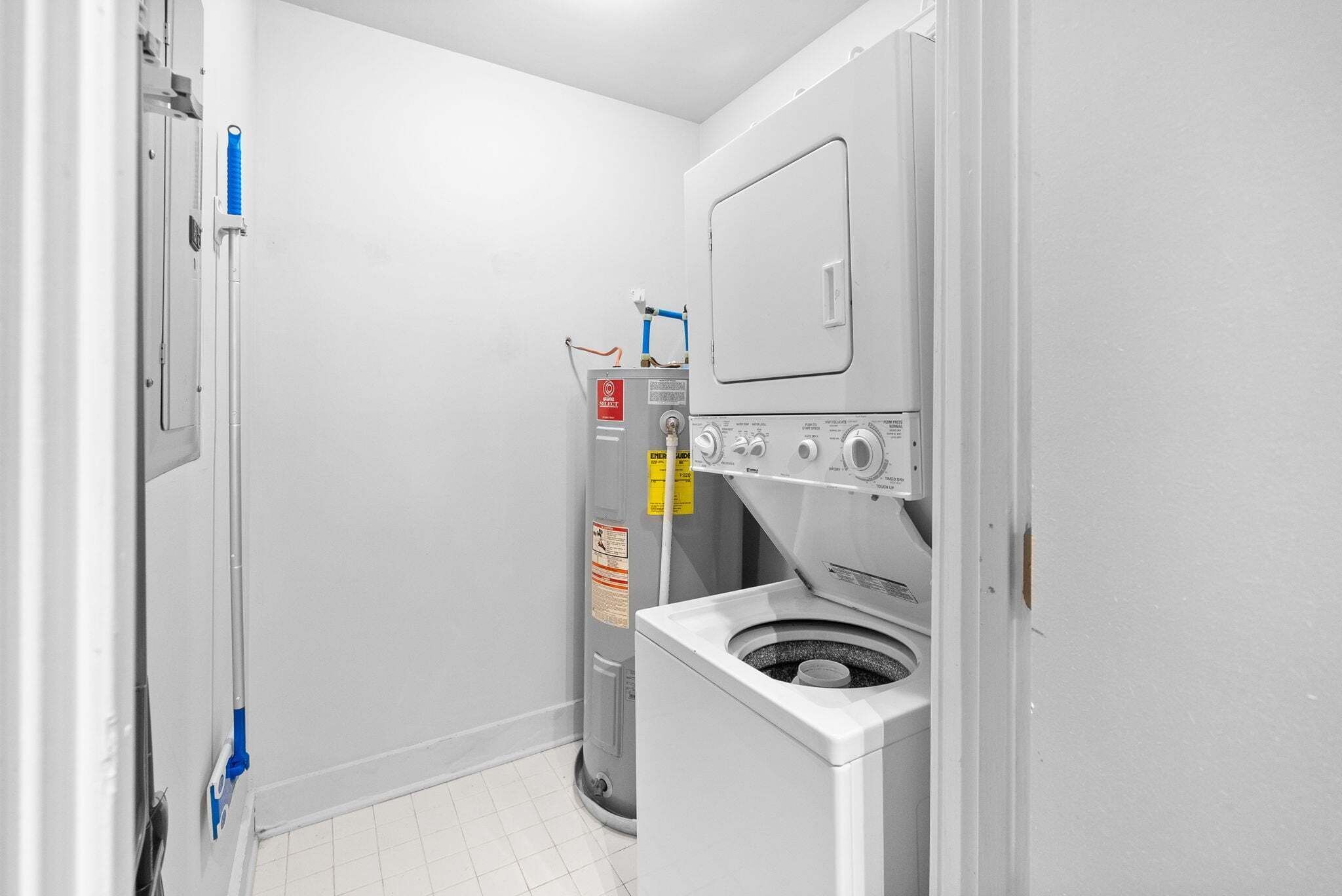 A compact laundry room with a washer and dryer, a water heater, and a mop.