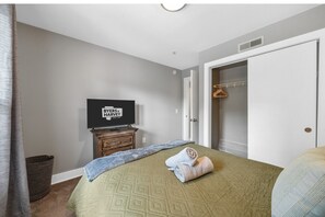 Une chambre à coucher avec un lit, un téléviseur posé sur un meuble en bois, une armoire et une porte donnant sur une autre pièce.