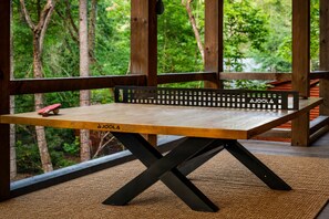 A ping pong table with a black frame and a wooden surface, placed on a textured mat. - Hemlock Social: Creekside Paradise • Pool • Sauna • HotTub • FirePit • Fun Games (Blue Ridge)