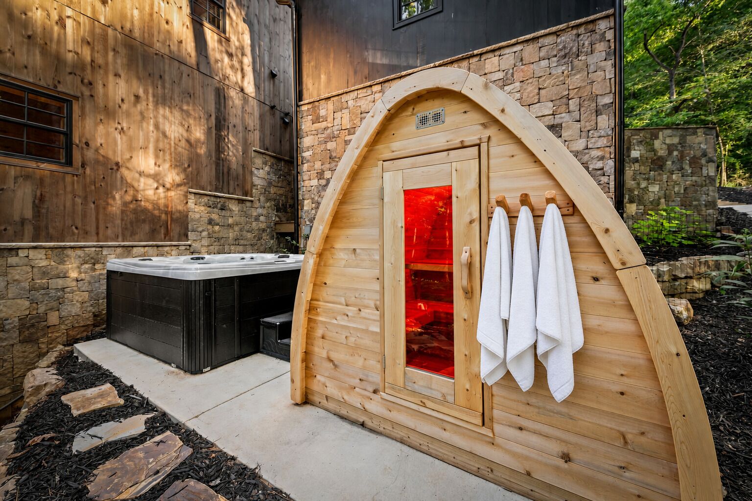 A sauna with a wooden exterior, a stone wall, and a hot tub in the background.