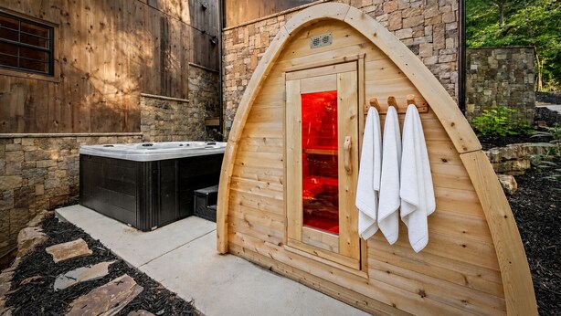 Uma sauna com fachada de madeira, parede de pedra e uma banheira de hidromassagem ao fundo.
