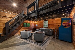 A log cabin interior with a staircase, seating area, and a Nintendo Donkey Kong arcade machine. - Hemlock Haven: Creekside Paradise • Pool • Sauna • HotTub • FirePit • Fun Games (Blue Ridge)
