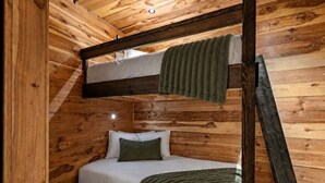 Uma cama beliche com teto e paredes de madeira, uma cama de solteiro embaixo e uma escada.