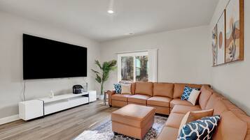 Una sala de estar moderna con un televisor de pantalla plana grande, un sofá de cuero, un mueble de entretenimiento blanco y una alfombra estampada.